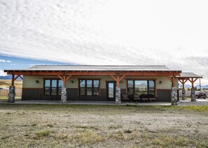 A lodge with a covered patio, stone pillars, and a view of the surrounding landscape.