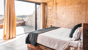 A bedroom with a large bed, wooden headboard, and a view through a sliding door to an outdoor area. - Vineyard Desert House -CuatroCuatros-CasaUno (Ensenada)