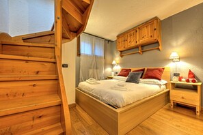 Escada de madeira que leva a uma cama com cabeceira, mesa de cabeceira e armário fixado na parede.