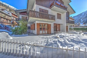 A multi-story building with wooden balconies, a snow-covered ground, and a mountainous backdrop.