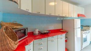 Une cuisine avec des meubles blancs, un plan de travail rouge, un four à micro-ondes, une bouilloire et une cuisinière.