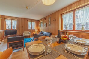 A cozy room with a dining table set for two, a sofa, a TV, and a window with curtains. - APT CAMILLE (Courmayeur)
