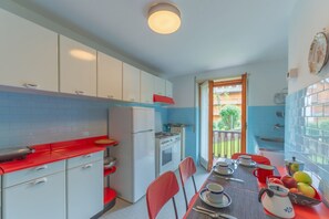 A compact kitchen with white cabinets, a red countertop, and a dining area with a table set for two. - APT CAMILLE (Courmayeur)
