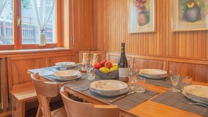 Une salle à manger aux murs lambrissés, avec une table dressée pour quatre personnes, comprenant assiettes, verres et une bouteille de vin.
