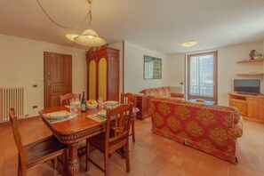 A dining area with a wooden table and chairs, a sofa, a television, and a window with a view.