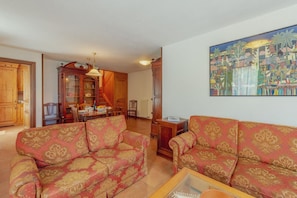 A living room with two patterned sofas, a dining table, and a kitchen area with wooden cabinets.