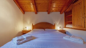 Ein Schlafzimmer mit Holzbalkendecke, einem großen Bett mit weißer Bettwäsche, zwei Nachttischen mit Lampen und einem Holzschrank.