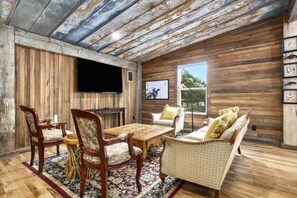A rustic interior with wooden walls, a flat-screen TV, a dining table with chairs, and a sofa.