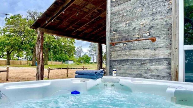 Un jacuzzi en un entorno exterior con una terraza de madera y un edificio rústico al fondo.