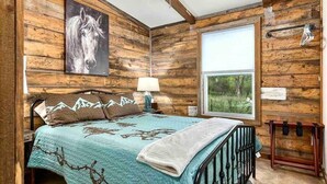 Una habitación rústica de madera con una cama, un ventanal con vistas a la vegetación y un cuadro de un caballo en la pared.