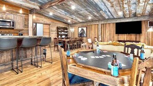 Un interior rústico con una mesa de comedor de madera, taburetes de bar y un rincón de estar acogedor.