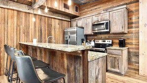 Una cocina rústica con paredes de madera, encimera de granito, refrigerador de acero inoxidable, microondas, estufa y taburetes de bar.