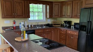 A kitchen with wooden cabinets, a granite countertop, a black refrigerator, and a window with a view of greenery. - Mountain Hideaway  (Ronceverte)