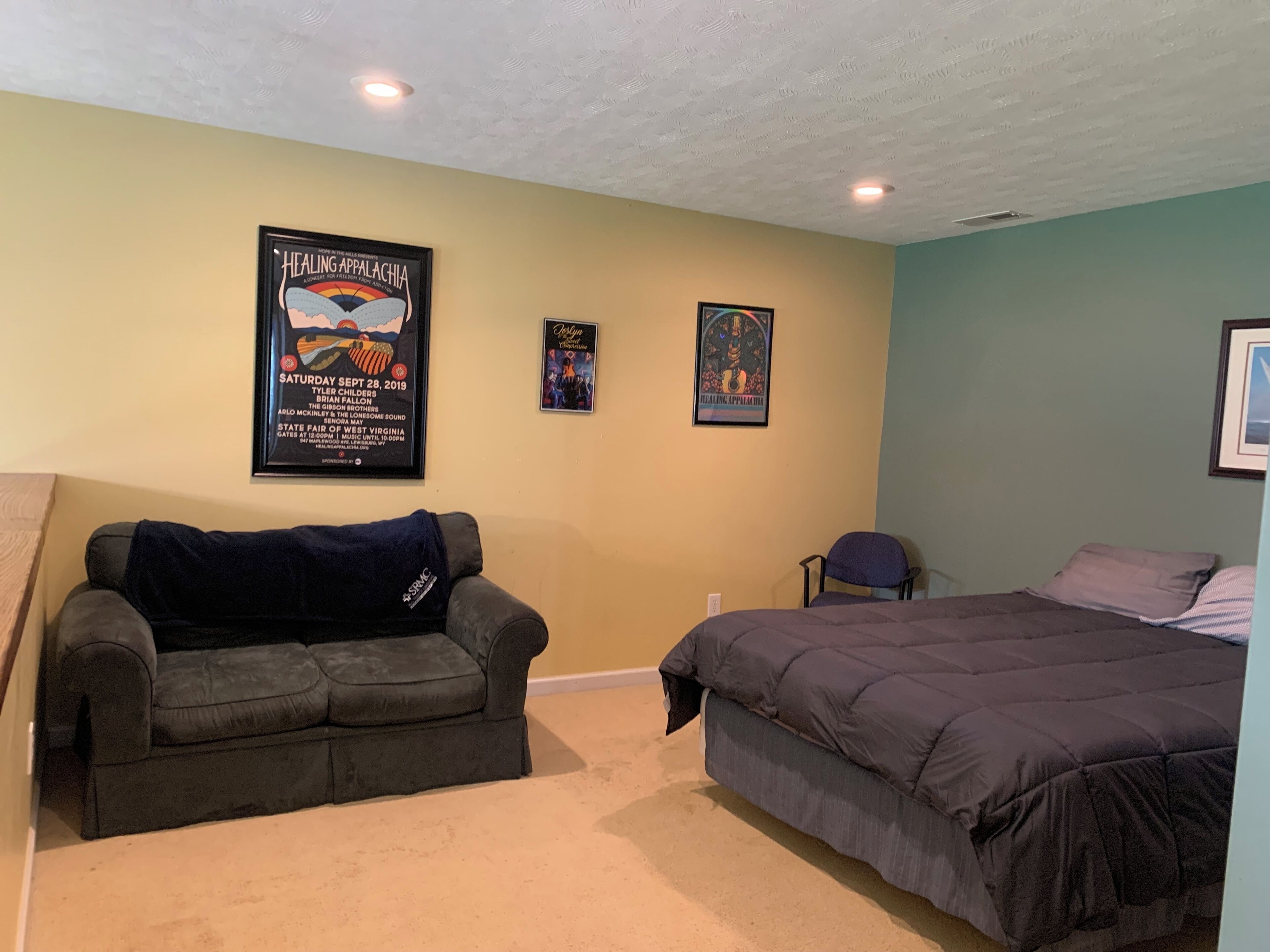A room with a couch, a bed, and two posters on the wall.