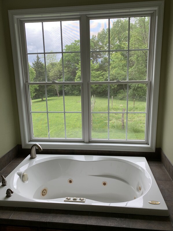 Ein Badezimmer mit einem großen Fenster, einer Badewanne und Blick auf eine grüne Landschaft.