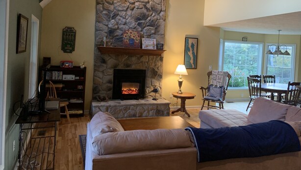 A cozy living room with a stone fireplace, a comfortable sofa, a dining area with a table and chairs, and a bookshelf. - Mountain Hideaway  (Ronceverte)