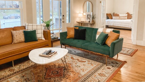Ein Wohnzimmer mit einem grünen Sofa, einem braunen Sofa, einem Couchtisch und einem Teppich.