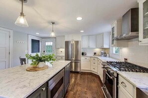 Cocina moderna con armarios blancos, refrigerador de acero inoxidable, estufa a gas y encimera de madera con una planta.