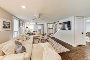 A spacious living room with a large sofa, a ceiling fan, and a staircase leading to another level. - Captain Cook, Hot Tub, Sleeps 9 (Lake Geneva)
