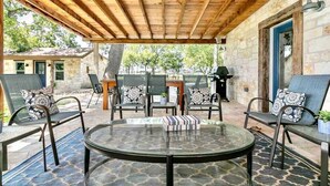 Ein überdachter Patio-Bereich mit einem runden Glastisch, Stühlen mit gemusterten Kissen und einer Steinmauer.