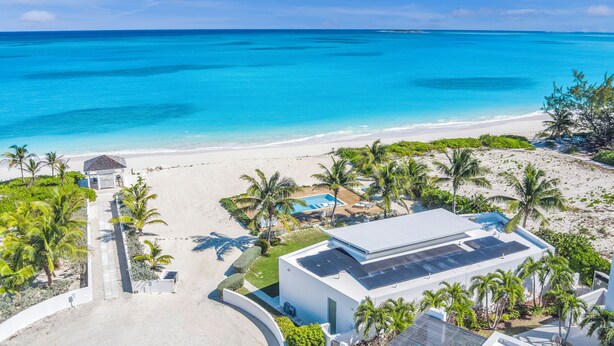 Une propriété située en bord de mer, dotée d’une piscine, de panneaux solaires et de palmiers.