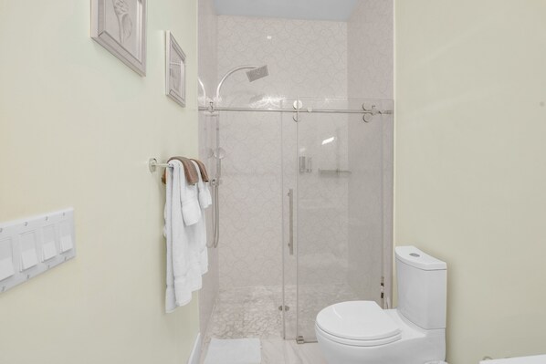 Ein modernes Badezimmer mit einer Glastrennwand-Dusche, einer weißen Toilette und einem Handtuchhalter mit Handtüchern.