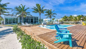 Une terrasse en bois avec une piscine, des chaises longues et des palmiers.