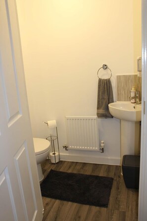 A small bathroom with a toilet, a radiator, a sink, and a dark rug on the floor. - 1-bed House - Sleeps 2 - Parking, Wifi (Peterborough)
