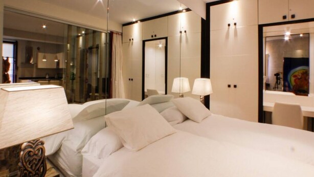 A modern hotel room with a large bed, bedside lamps, a mirror, and a view of the bathroom. - Suite Bali by RentalSevilla (Sevilla)