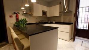 A modern kitchen with white cabinets, a black countertop, and a stainless steel range hood. There is a plant on the island, and a fire extinguisher mounted on the wall. - Suite Bali by RentalSevilla (Sevilla)