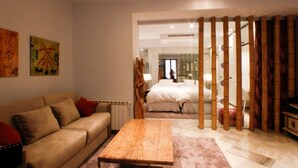 A modern living room with a sofa, a wooden coffee table, and a bed in the background. - Suite Bali by RentalSevilla (Sevilla)