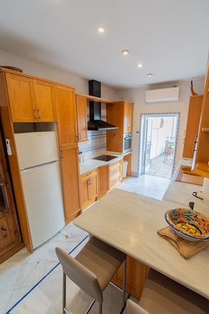 A modern kitchen with wooden cabinets, a white countertop, and a dining area with a table and chairs.