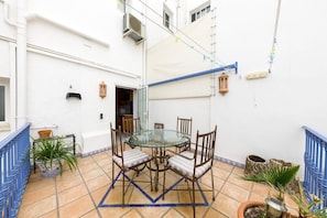 A glass-top table with four chairs, a blue railing, and potted plants on a tiled patio.