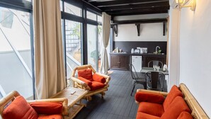 A cozy room with a dining area and kitchen, featuring wicker furniture and a view through large windows. - Terraza Tailandia by Rentalsevilla (Sevilla)