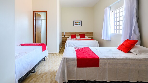 A hotel room with two beds, a wooden headboard, a window with curtains, and a door. - Tropical Brisa (São Sebastião)