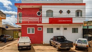 A two-story building with a red and white facade, a sign reading "HOTEL BRISA TROPICAL," and several parked vehicles in front. - Tropical Brisa (São Sebastião)