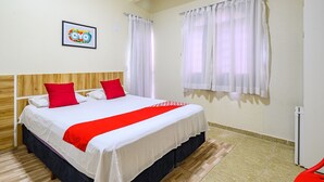 A hotel room with a bed, red pillows, a white bedspread, a framed picture on the wall, and white curtains on the windows. - Tropical Brisa (São Sebastião)