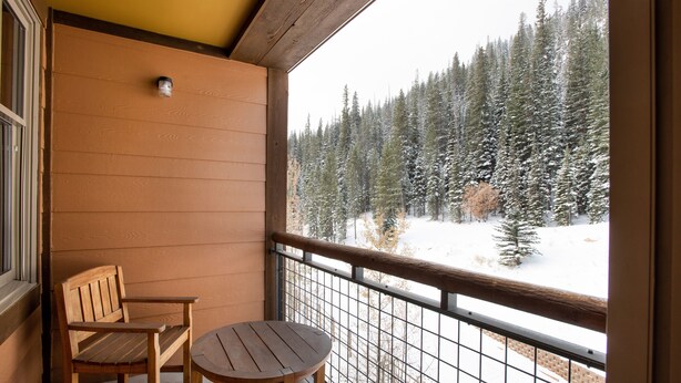 Un balcón con banco y mesa de madera, con vistas a un bosque nevado.
