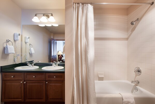 A bathroom with two sinks, a mirror, a hairdryer, and a bathtub.