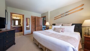 Une chambre avec un grand lit, une commode, un téléviseur, un miroir et un porte-skis fixé au mur.