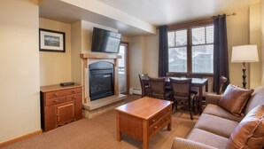 A living room with a fireplace, a television, a dining table with chairs, and a sofa. - Zephyr Mountain Lodge, Condo | 4th Floor Tucked Into The Woods Ski-In/Ski-Out (Select-Rated Condo 1402) (Winter Park)