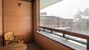 A balcony with a wooden chair and a view of buildings covered in snow. - Zephyr Mountain Lodge, Condo | 4th Floor Tucked Into The Woods Ski-In/Ski-Out (Select-Rated Condo 1402) (Winter Park)