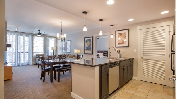 A modern kitchen with a central island, dining area with chairs, and a large window with blinds. - Fraser Crossing/Founders Pointe, Condo | 2 Bedroom (Value-Rated Condo 4281) (Winter Park)