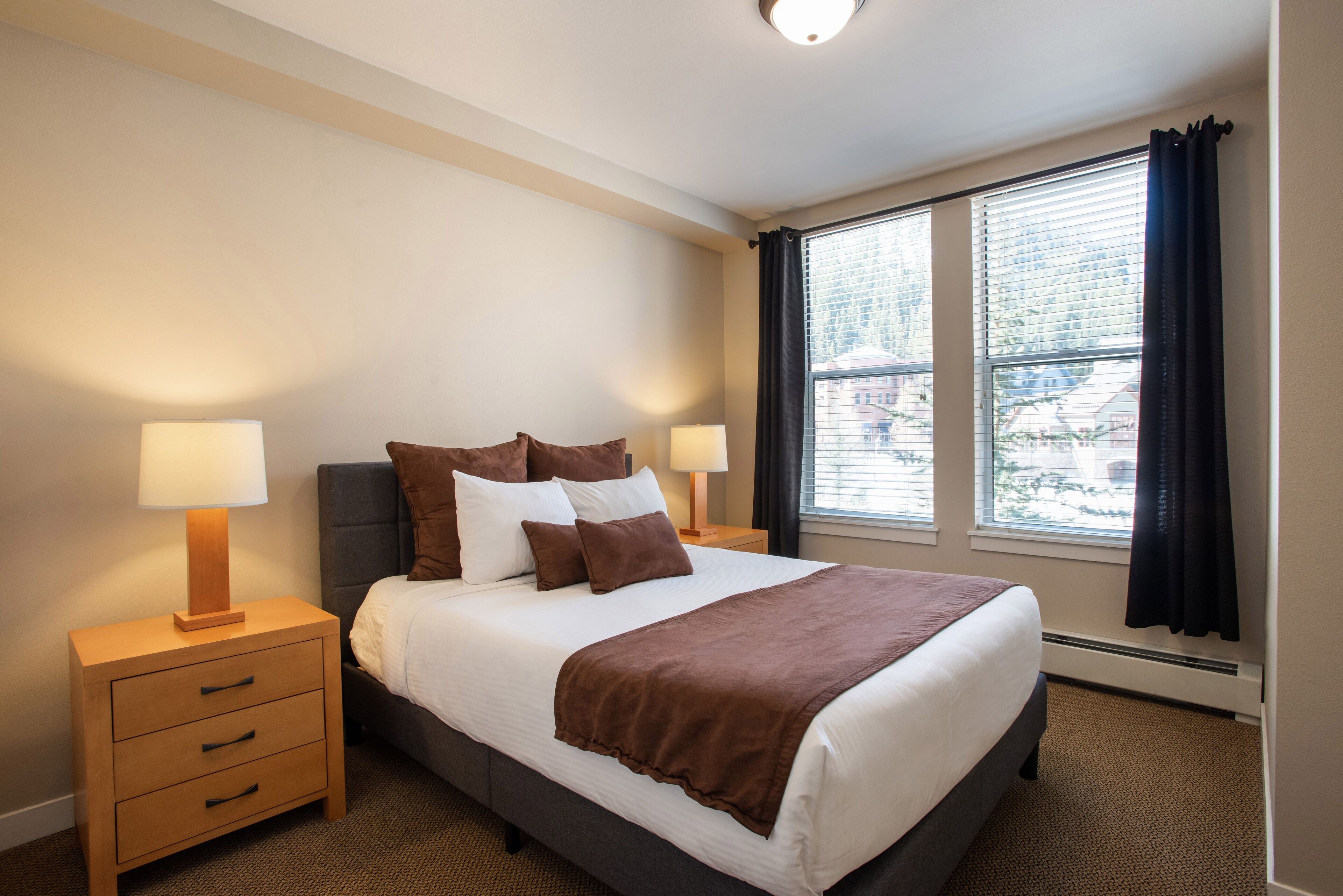 A neatly made bed with a brown blanket, two bedside lamps, and a nightstand with drawers.