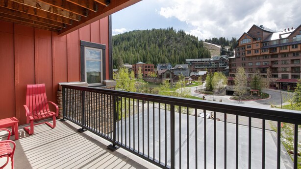 A balcony with red chairs, a view of a town with buildings and a forested hill. - Fraser Crossing/Founders Pointe, Condo , Ski Slope View (Premium-Rated Condo 4340) (Winter Park)