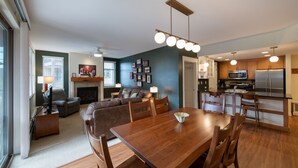 A modern living room with a fireplace, a dining area with a wooden table and chairs, and a kitchen with stainless steel appliances. - Fraser Crossing/Founders Pointe, Condo , Ski Slope View (Premium-Rated Condo 4340) (Winter Park)
