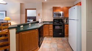 A modern kitchen with wooden cabinets, a stainless steel microwave, a black oven, and a white refrigerator. - Zephyr Mountain Lodge, Condo | 2 bedroom Ski Slopes Balcony Views (Value Rated Condo 2411) (Winter Park)