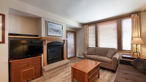 A living room with a television, fireplace, sofa, and windows with blinds. - Zephyr Mountain Lodge, Condo | 2 bedroom Ski Slopes Balcony Views (Value Rated Condo 2411) (Winter Park)