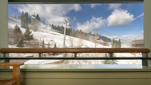 Une fenêtre donnant sur un paysage montagneux enneigé, avec notamment un télésiège et des arbres.