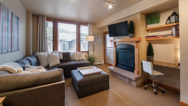 A modern living room with a sofa, ottoman, fireplace, television, and bookshelves. - Zephyr Mountain Lodge, Condo | 2 Bedroom (Select-Rated Condo 2406) (Winter Park)